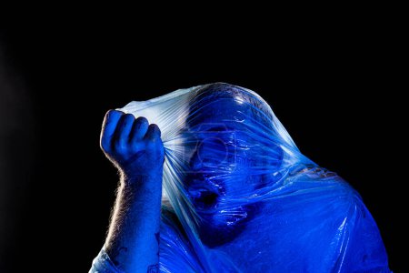 Foto de Hombre con bolsa de plástico en la cabeza, asfixiado. Estudio con filtro azul. Aislado sobre fondo negro. - Imagen libre de derechos