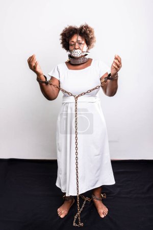 Téléchargez les photos : Portrait d'une femme noire enchaînée avec un masque de fer sur la bouche. Esclavage au Brésil. Les armes dans la prière. Reproduction studio. - en image libre de droit