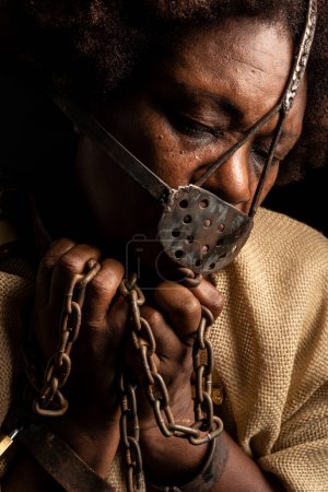 Photo for Close-up portrait of a black woman with chains on her hands and an iron mask on her face. Slave Anastacia. Slavery in Brazil. - Royalty Free Image