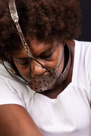 Téléchargez les photos : Femme noire enchaînée avec un masque de fer sur le visage, représentant l'esclave Anastacia. Douleur et souffrance, torture. Sur fond noir. - en image libre de droit