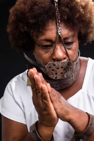 Photo for Portrait of the face of a black woman with an iron mask on her face, representing the slave Anastacia. Praying for less pain. Slavery in Brazil. - Royalty Free Image