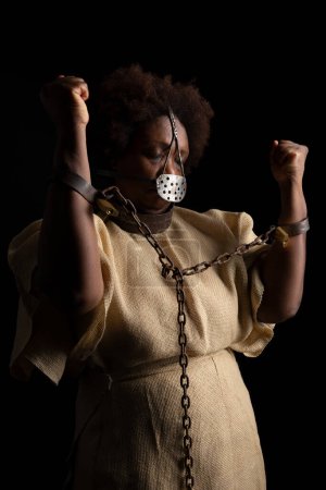 Téléchargez les photos : Portrait d'une femme noire portant un masque de fer sur son visage pour représenter la douleur de l'esclave Anastacia. Isolé sur fond noir - en image libre de droit