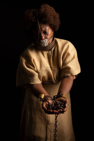 Photo for Portrait of a black woman in chains and with an iron mask on her face holding chains. Slave Anastacia. Slavery in Brazil. - Royalty Free Image