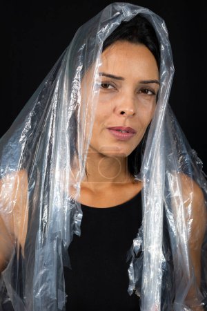Foto de Una mujer con una bolsa de plástico sobre su cabeza en forma de velo. Protesta contra el uso de plástico. Problemas ambientales. Aislado sobre fondo negro. - Imagen libre de derechos
