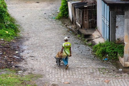 Téléchargez les photos : Aratuipe, Bahia, Brésil - 31 août 2018 : Un résident de Maragogipinho charge des matériaux dans une brouette dans les rues de la ville d'Aratuipe, Bahia. - en image libre de droit