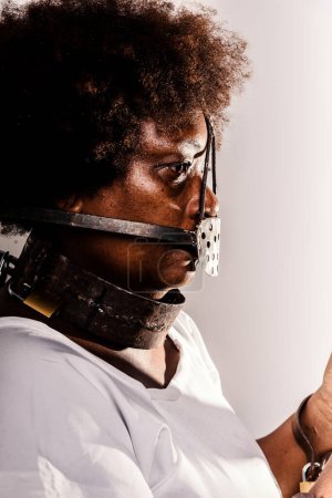 Photo for Profile portrait of black woman with iron mask of slavery on her mouth. Rusty iron material. Studio reproduction. - Royalty Free Image
