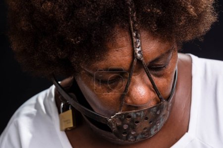 Photo for Portrait of the face of a black woman with an iron mask on her face, representing the slave Anastacia. Pain and suffering, torture. Against black background. - Royalty Free Image