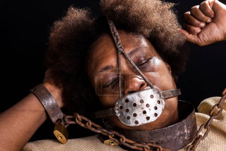 Photo for Portrait of a black woman in chains with an iron mask on her face representing the slave Anastacia. Slavery in Brazil. Isolated on black background. - Royalty Free Image