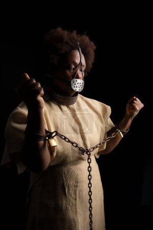 Photo for Portrait of a black woman wearing an iron mask on her face to represent the pain of the slave Anastacia. Isolated on black background - Royalty Free Image
