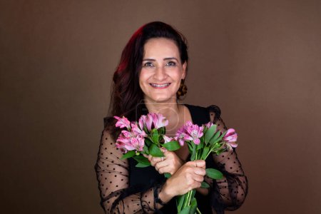 Photo for Beautiful woman in black clothes holding a bouquet of flowers. In love and happy. Isolated on brown background. - Royalty Free Image