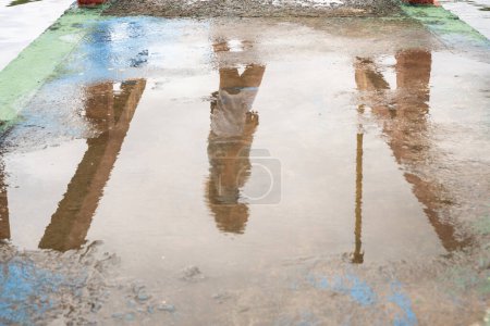 Téléchargez les photos : Réflexion d'une personne non identifiée dans la flaque d'eau sur le sol en ciment. Photo abstraite, fond et texture. - en image libre de droit