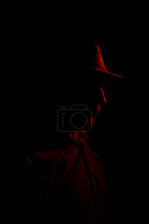 Foto de Hombre con sombrero sobre fondo oscuro, con gafas de sol con luz roja en la cara. Retrato de estudio - Imagen libre de derechos