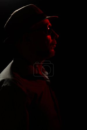 Foto de Hombre con sombrero sobre fondo oscuro, con gafas de sol con luz roja en la cara. Retrato de estudio - Imagen libre de derechos