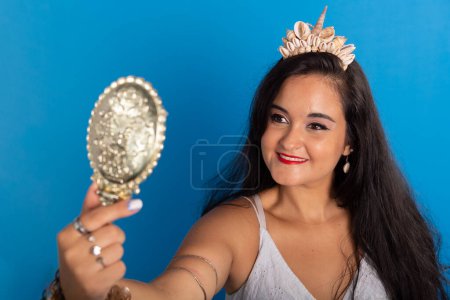 Photo for Portrait of beautiful black-haired woman wearing white clothing, smiling, holding and looking into a mirror. Devotee of iemanja. - Royalty Free Image