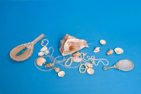 Photo for Several sea shells, necklaces and mirror scattered on the blue studio floor. Tribute to iemanja. - Royalty Free Image