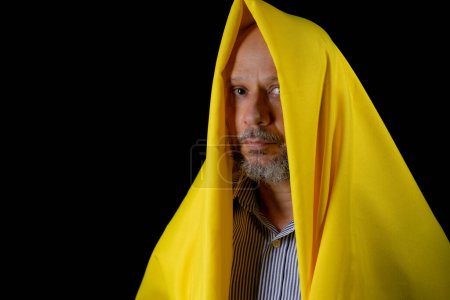 Photo for Bald, bearded man with a yellow cloth over his head against black background. - Royalty Free Image