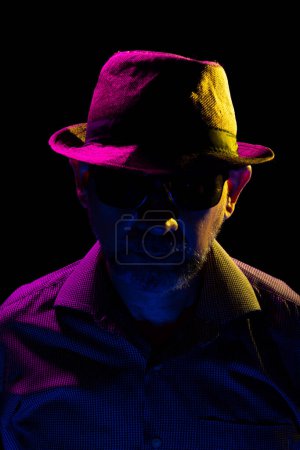 Foto de Un hombre misterioso con sombrero y gafas de sol. Retrato en estudio oscuro. - Imagen libre de derechos