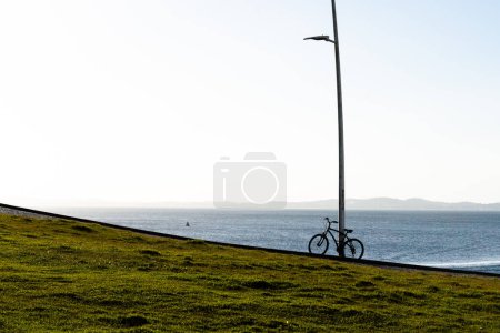 A bicycle parked against a lamppost against the sea in the background. Bay of All Saints