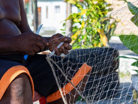 Téléchargez les photos : Santo Amaro, Bahia, Brésil - 01 juin 2019 : Un pêcheur est vu assis et réparant un filet de pêche à Acupe, district de Santo Amaro à Bahia. - en image libre de droit