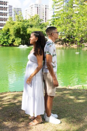 Téléchargez les photos : Couple avec le dos à l'autre. En arrière-plan une lagune verte. Elle est enceinte. Genre révélé. - en image libre de droit