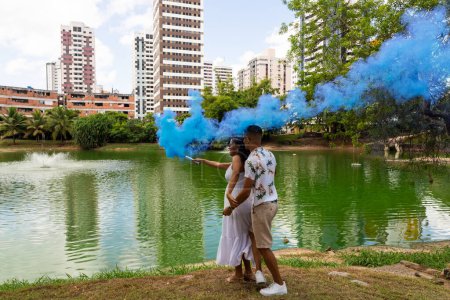 Téléchargez les photos : Joyeux couple ayant une fête révélatrice de genre. grenade de fumée bleue à l'extérieur. C'est un garçon. Le genre révèle le concept du parti. Couple amoureux - en image libre de droit