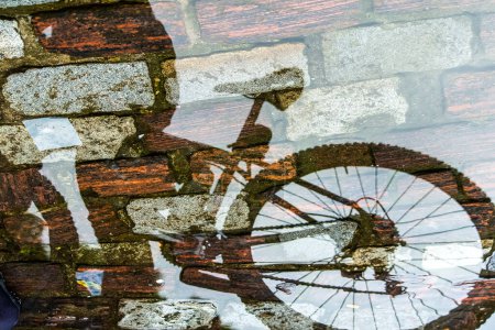 Reflexion von Person und Fahrrad in einer Pfütze aus Regenwasser im Fluss. Abstrakte Unschärfe.