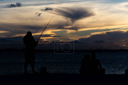 Foto de Salvador, Bahia, Brasil - 13 de abril de 2019: Pescador es visto en silueta durante la puesta de sol en Ponta do Humaita en la ciudad de Salvador, Bahia. - Imagen libre de derechos