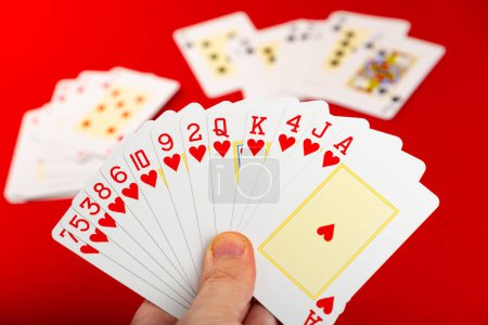 Spielkarten. Pokerkarten in der Hand eines Enthusiasten. Brettspiel. Vereinzelt auf rotem Hintergrund.