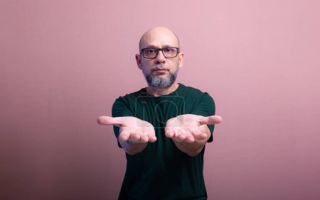 Bearded bald man with prescription glasses showing his palm. Isolated on salmon colored background.