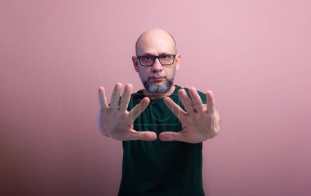 Portrait of bald, bearded man wearing prescription glasses showing his palm. Isolated on salmon colored background.
