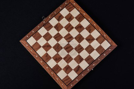 Foto de Tablero de madera vacío de una partida de damas o ajedrez fotografiado desde arriba sobre un fondo negro. - Imagen libre de derechos