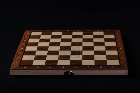 Foto de Tablero de madera vacío de una partida de damas o ajedrez sobre fondo negro. - Imagen libre de derechos