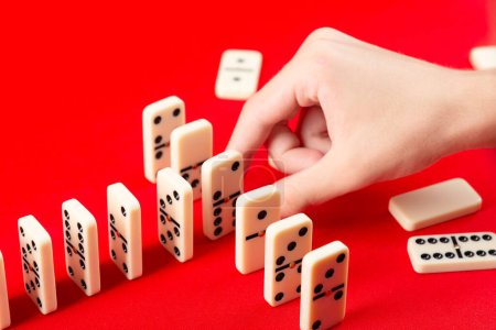 Männliche Hand legt die Figuren hintereinander für den Dominoeffekt. Vereinzelt auf rotem Hintergrund.
