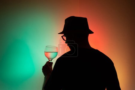 Porträt eines unbekannten Mannes in Silhouette, der ein Glas mit Flüssigkeit im Inneren hält. Isoliert auf farbigem Hintergrund.