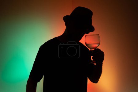 Portrait of an unidentified man in silhouette holding a glass with liquid inside. Isolated on colored background.