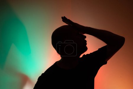 Studio portrait of a man in silhouette with his hand over his head. Isolated on colored background.
