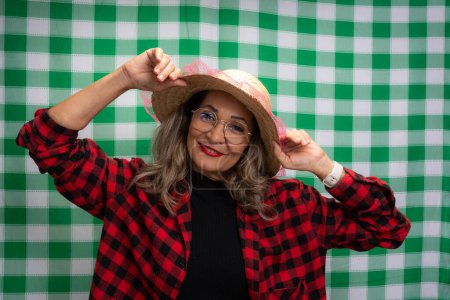 Portrait of a woman dressed for the Sao Joao festival wearing a straw hat and posing for a photo. Isolated on green and white checkered background.
