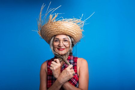 Beautiful woman dressed for the Sao Joao festival, standing, holding her hair braids and posing for a photo. Isolated on blue background.