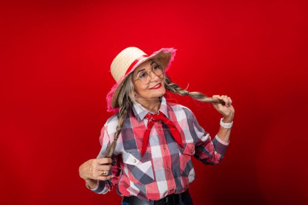 Beautiful woman, wearing a straw hat with typical clothing for the Sao Joao festival, holding her hair braids. Isolated on red background.