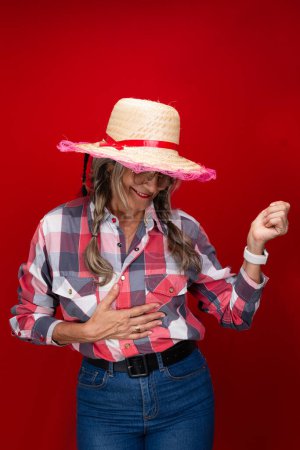 Beautiful woman, wearing a straw hat with typical clothing for the Sao Joao festival, posing and dancing. Isolated on red background.
