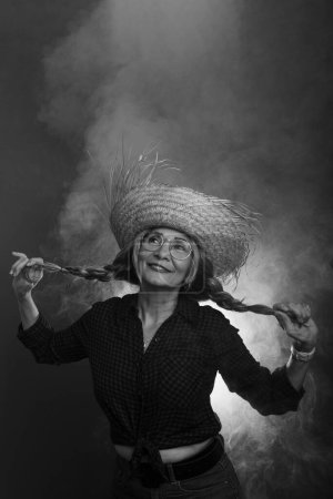 Portrait noir et blanc de belle femme aux cheveux tressés portant un chapeau de paille sur fond fumé.