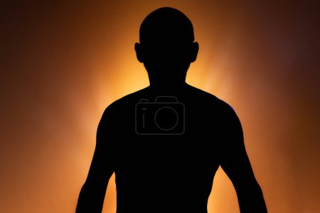 Man in silhouette, standing still and shirtless, posing for a photo. Isolated on orange color background.