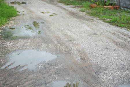 The road is wet with rainwater, has holes and is damaged.