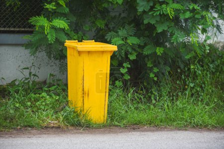 A yellow trash can sits on the side of the road.