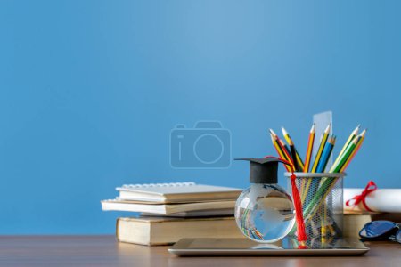 Téléchargez les photos : Journée de diplôme.Education concept d'apprentissage.Un mortier sur globe de cristal avec pile de livres et crayons de couleur dans un étui à crayons sur fond bleu. - en image libre de droit