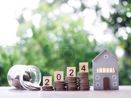 Wooden blocks with number 2024 on stack of coins and miniature house. The concept of saving money for house, Property investment, House mortgage, Real estste in New Year 2024.