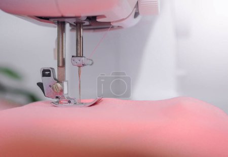 Téléchargez les photos : Gros plan de la machine à coudre travaillant avec du tissu rose, coudre de nouveaux vêtements. - en image libre de droit