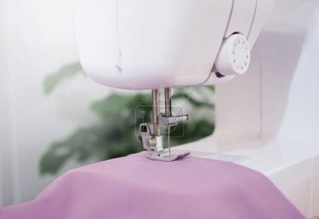 Téléchargez les photos : Gros plan de la machine à coudre travaillant avec du tissu violet, coudre de nouveaux vêtements. - en image libre de droit