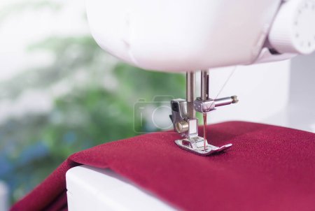 Téléchargez les photos : Gros plan de la machine à coudre travaillant avec du tissu rouge, coudre de nouveaux vêtements. - en image libre de droit