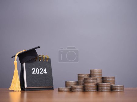 Téléchargez les photos : Objectifs d'étude, 2024 Calendrier de bureau avec chapeau de graduation et pile de pièces. Le concept d'économiser de l'argent pour l'éducation, prêt étudiant, bourse, frais de scolarité au Nouvel An 2024 - en image libre de droit